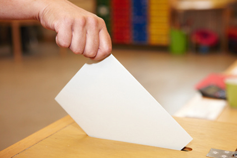 Ein Stimmzettel wird in eine Wahlurne eingeworfen.